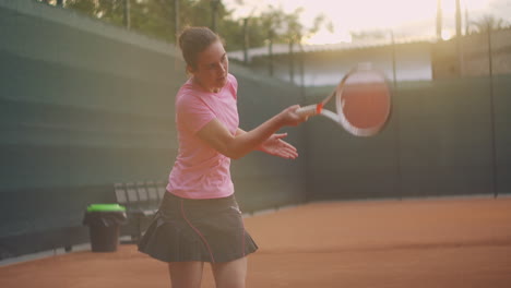 Young-woman-walking-through-tennis-court-with-racket.-Backside-view-of-attractive-brunette-female-in-blue-shirt-and-black-shorts-entering-tennis-hardcourt.-Full-length-follow-shot-with-copy-space